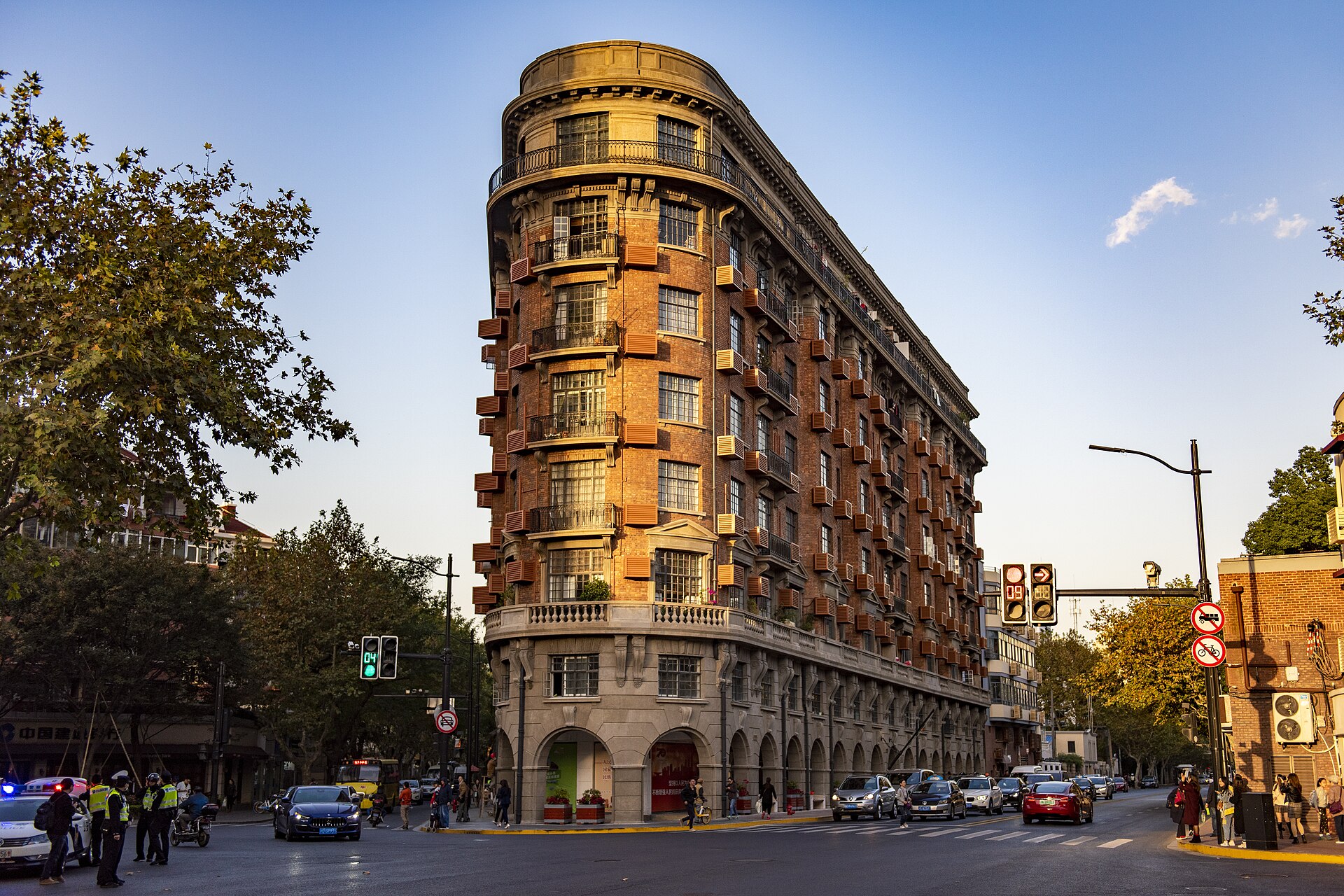 Wukang Mansion (武康大楼), the wedge-shaped 1924 landmark, glowing in golden-hour light above the plane-tree-lined streets of the former French Concession, Shanghai
