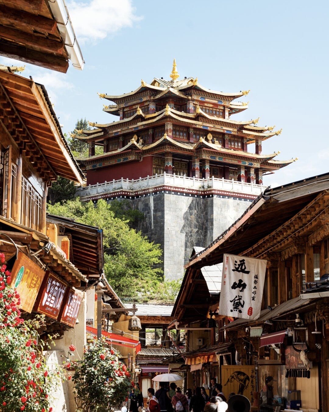 Golden-tiered Tibetan temple towering above the wooden shopfronts and flowering street of Shangri-La old town.