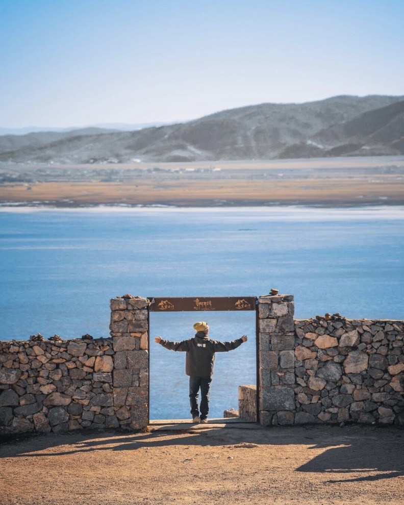 Person standing arms-outstretched in a stone-gate viewpoint overlooking the blue expanse of Napa Lake and distant hills near Shangri-La.