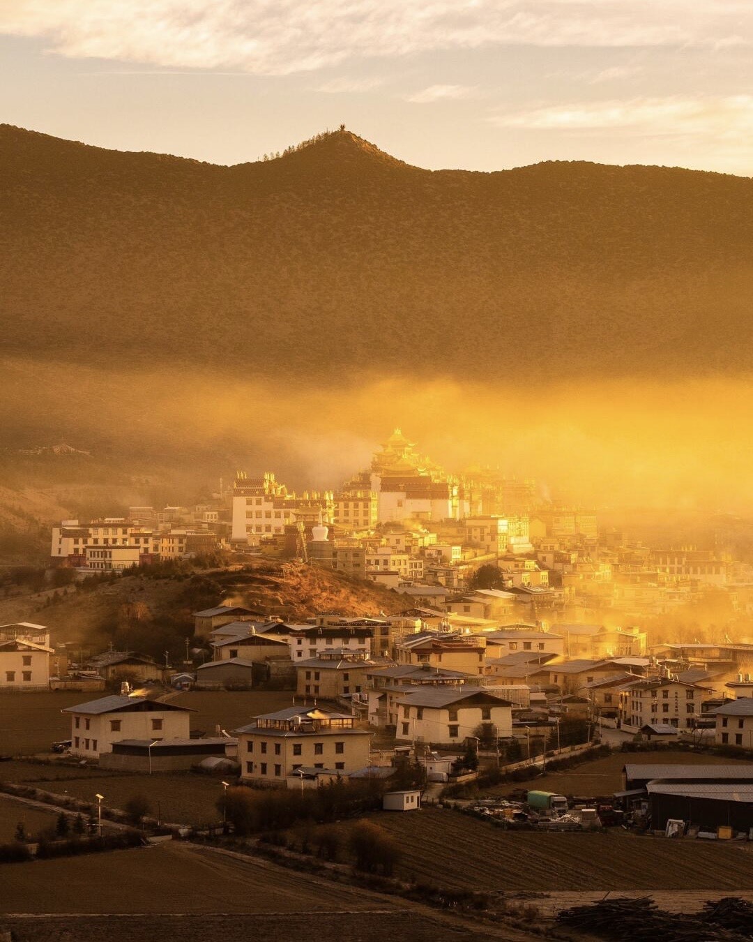 Songzanlin Monastery and its surrounding Tibetan village glowing in golden sunrise light and mist below a hillside near Shangri-La.