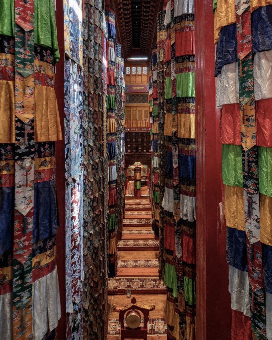 Ornate silk brocade hangings drape tall pillars along a narrow carpeted aisle inside Songzanlin Monastery near Shangri-la.