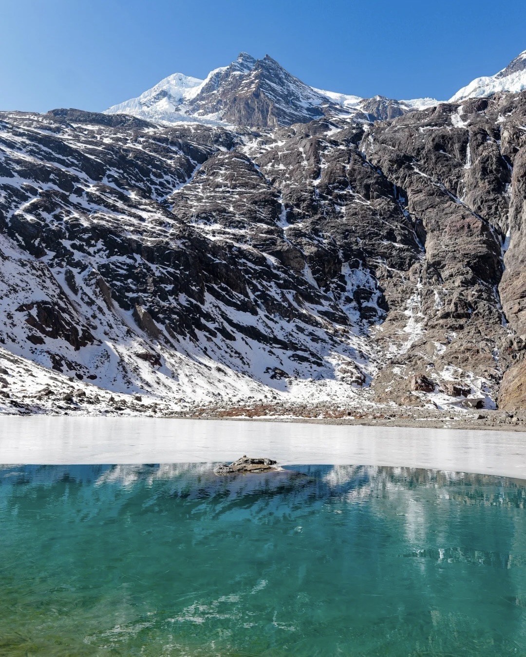 Turquoise glacial lake ringed by snow-streaked slopes below jagged white peaks on the Yubeng village trek near Shangri-La.