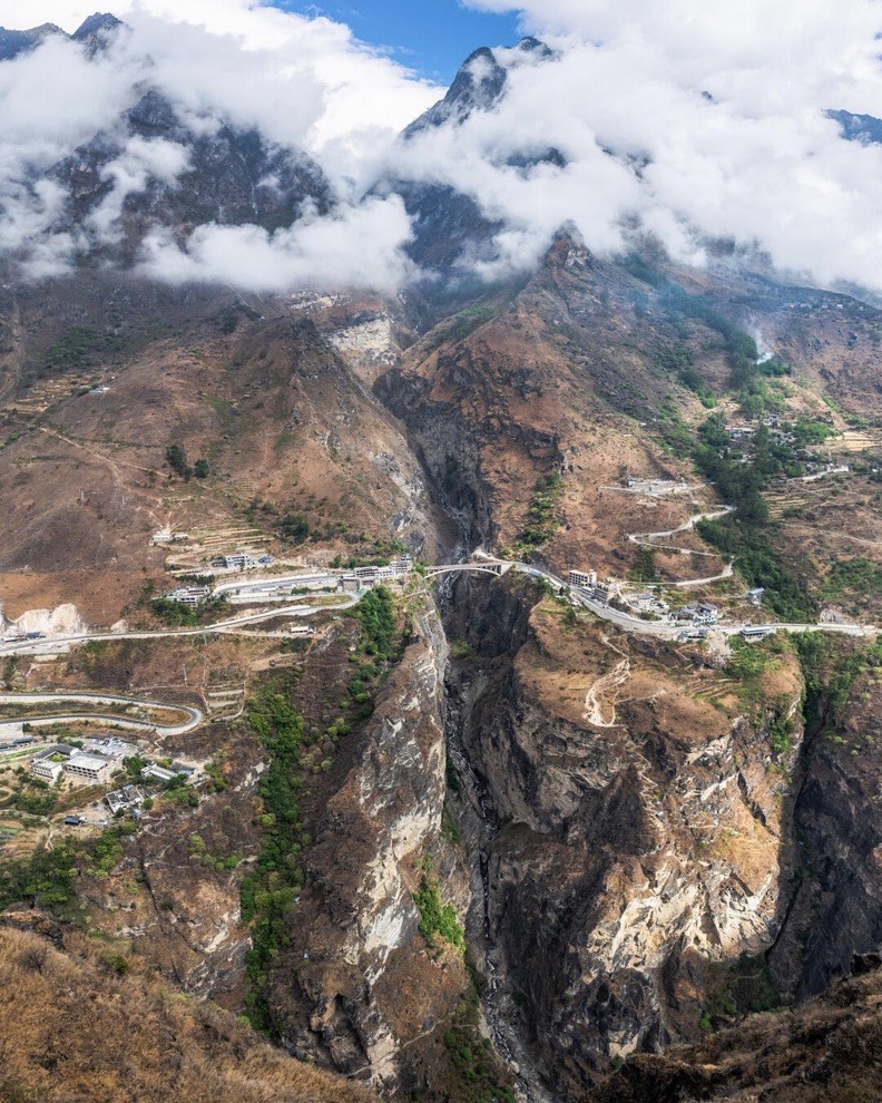 Aerial view of switchback roads and villages clinging to steep canyon slopes with clouds along Tiger Leaping Gorge.