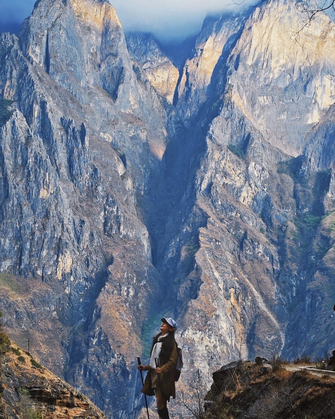 Hiker with trekking poles looking up at the steep striated canyon walls of Tiger Leaping Gorge near Shangri-La.