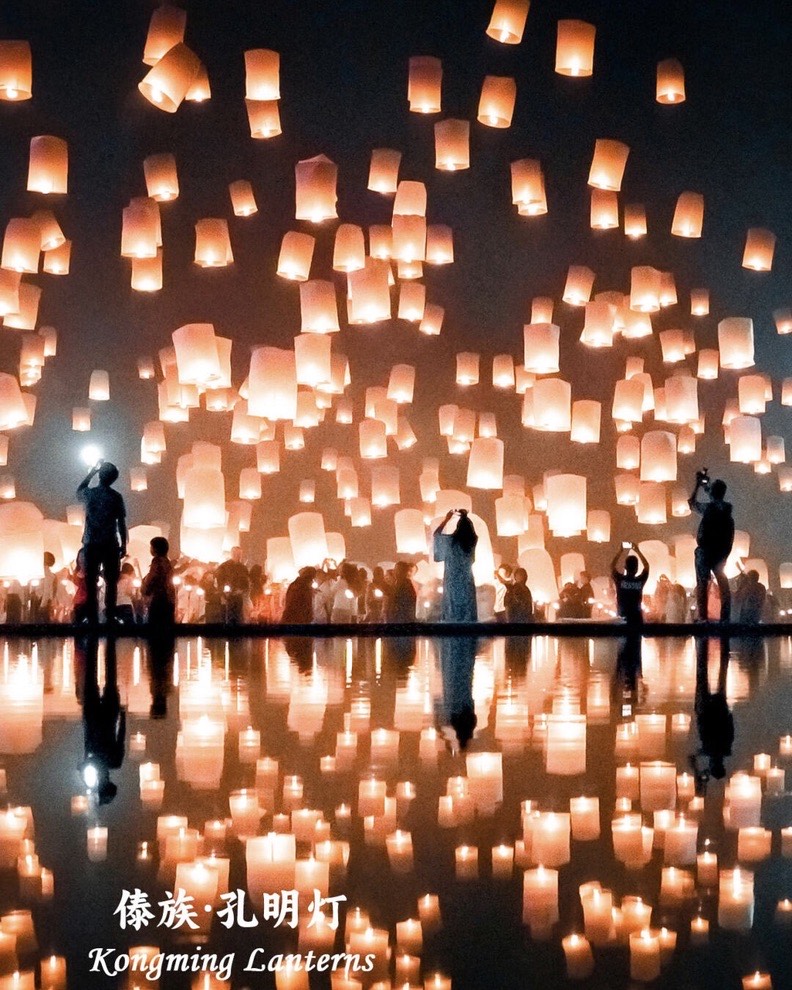 Crowds release glowing paper sky lanterns that fill the sky and mirror across still water at night.