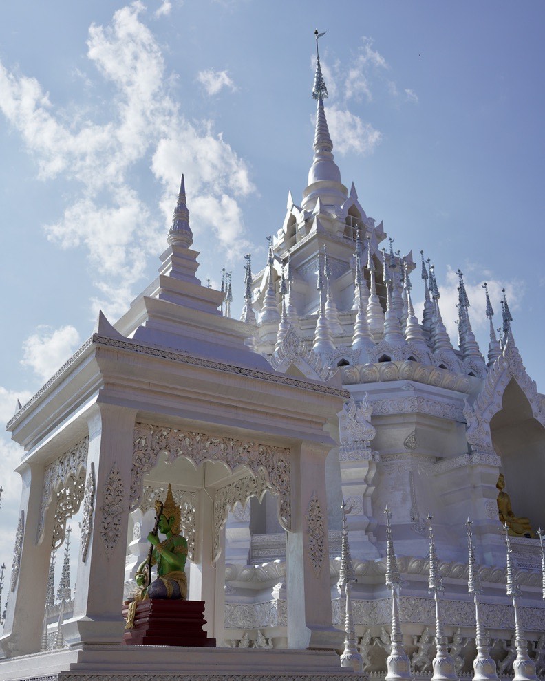 Ornate white Dai-style temple with pointed spires and a carved shrine holding a statue under blue sky.