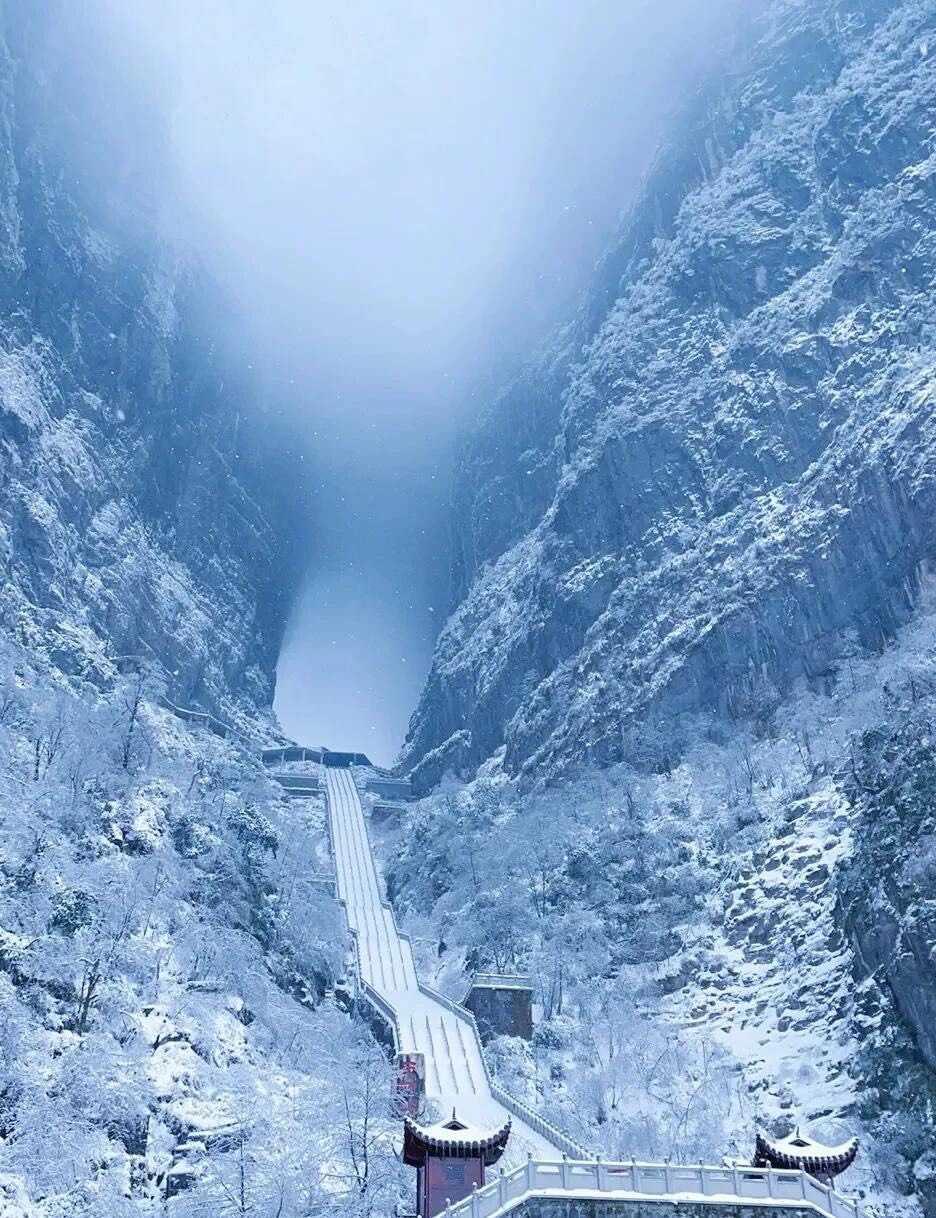 Snow blankets the steep stairway climbing toward the cliff-framed cave gate of Tianmen Mountain in winter.