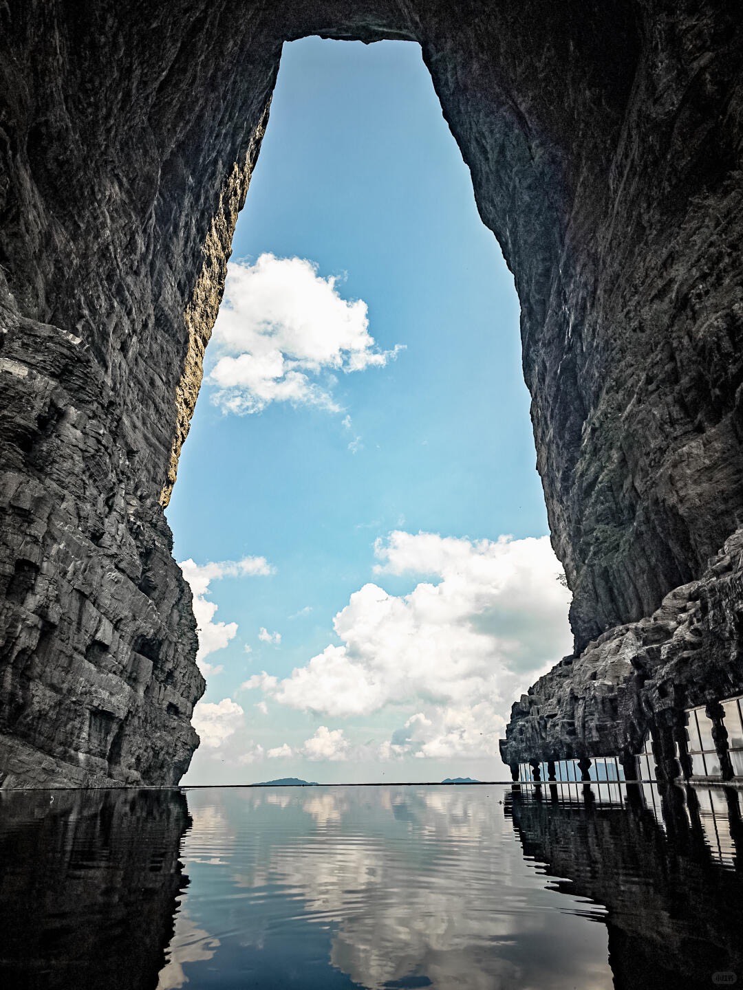 Towering cliffs framing a tall natural rock arch and blue sky mirrored in still water below at Tianmen Mountain.