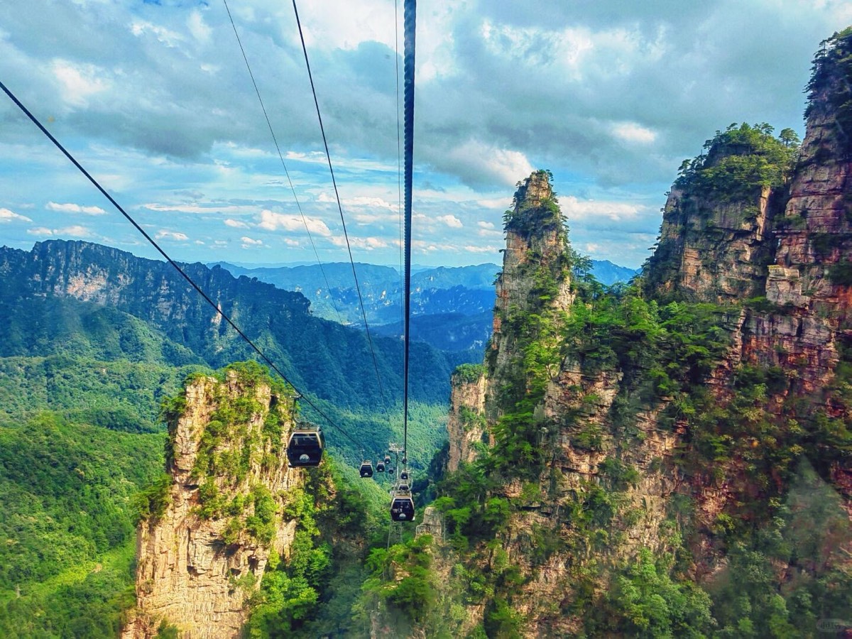 Cable-car gondolas gliding between forested quartzite sandstone pillars above green valleys at Wulingyuan, Zhangjiajie.