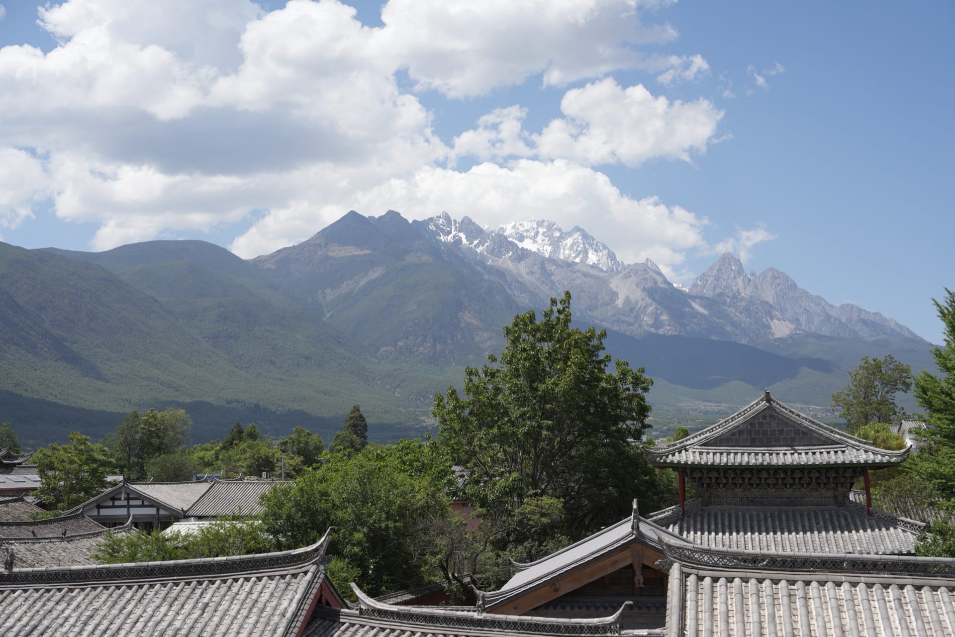 Jade Dragon Snow Mountain's peaks above the tiled Naxi rooftops of Lijiang under a blue sky — hero image for the Classic China & Yunnan tour by Boutique China