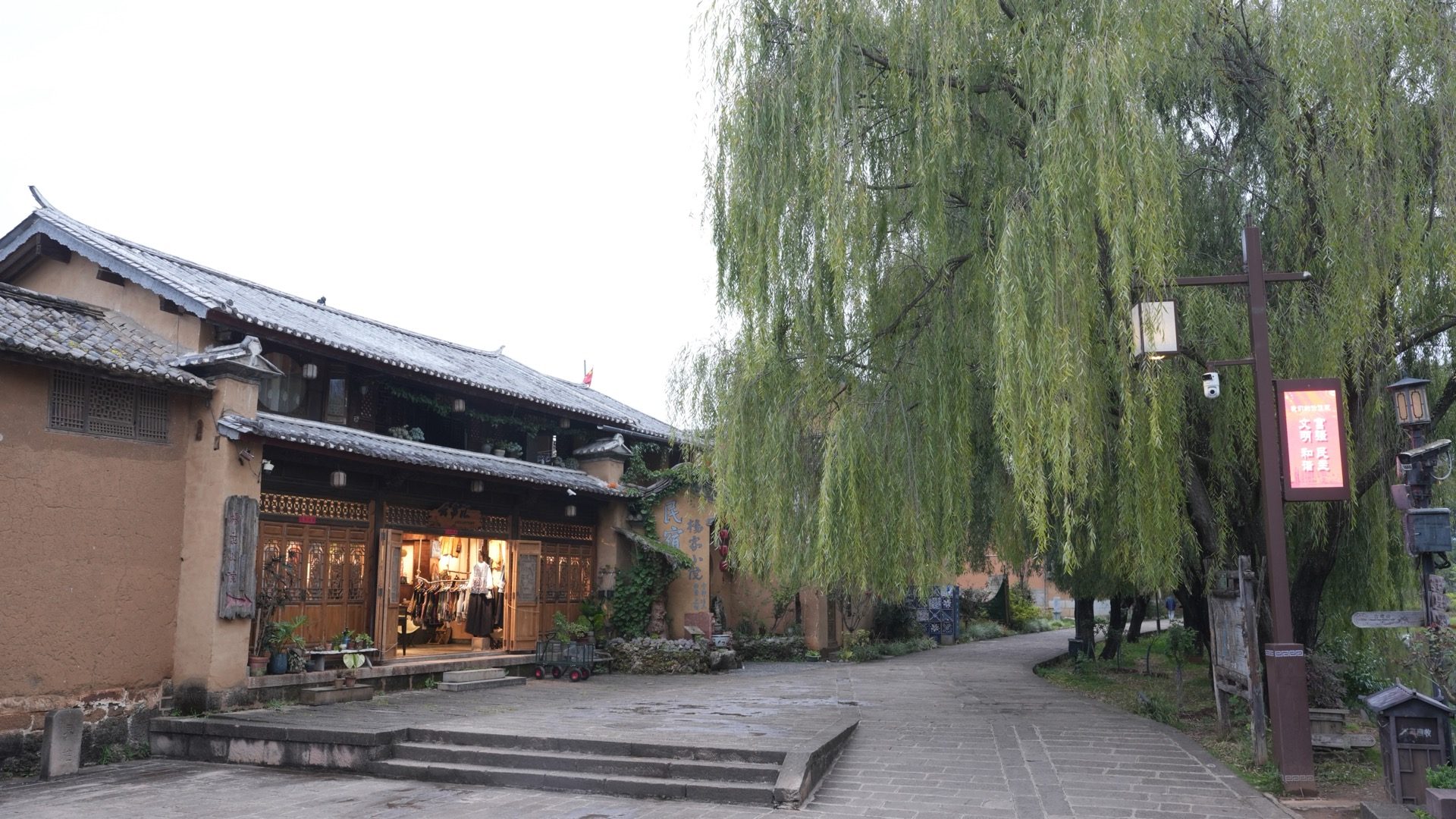 Weeping willow over a quiet Shaxi street with restored Bai courtyard storefronts at dusk