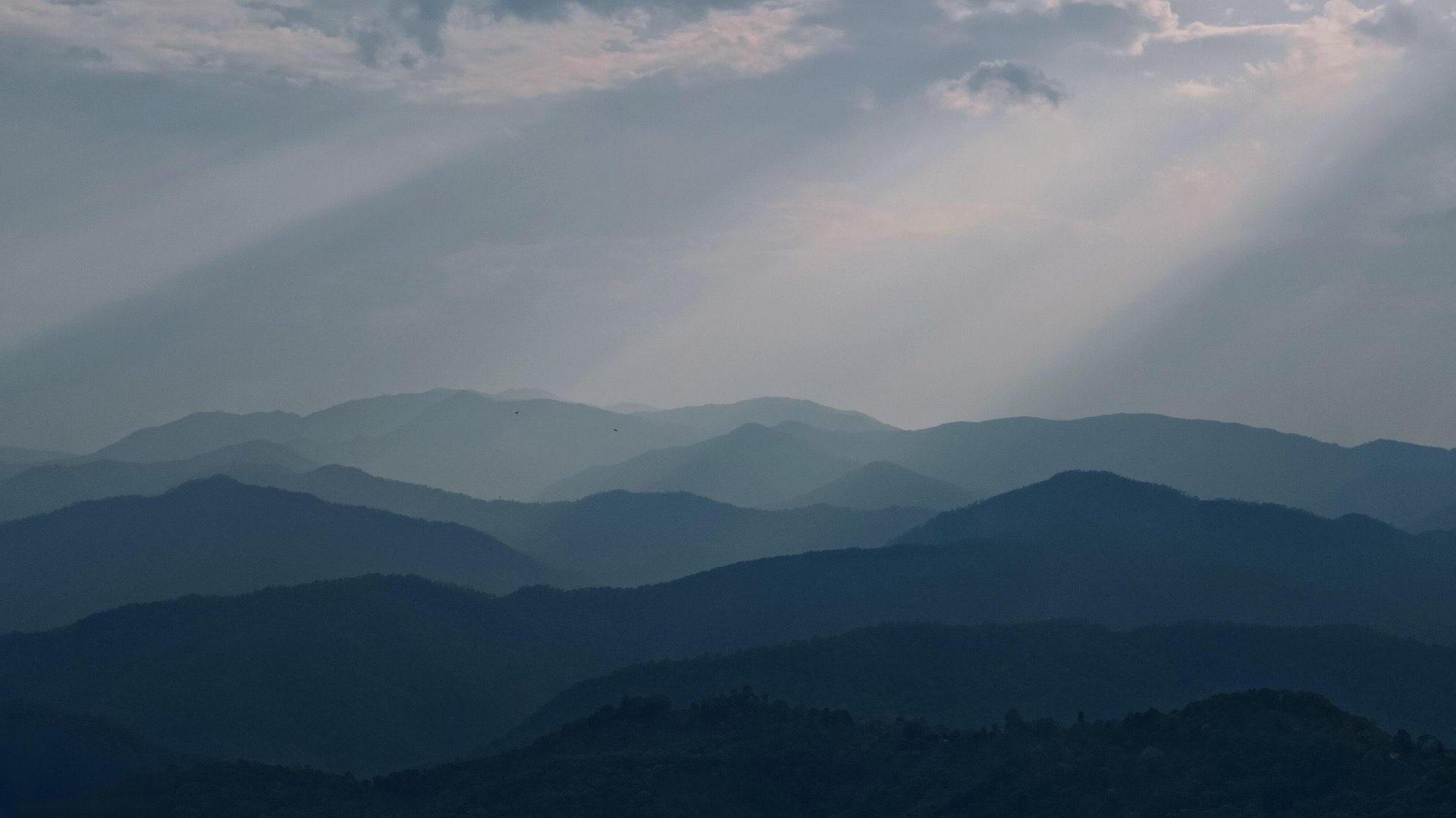 Layered misty mountain ridges with god-rays through the clouds over the Pu’er tea country — Tea Journeys hero image