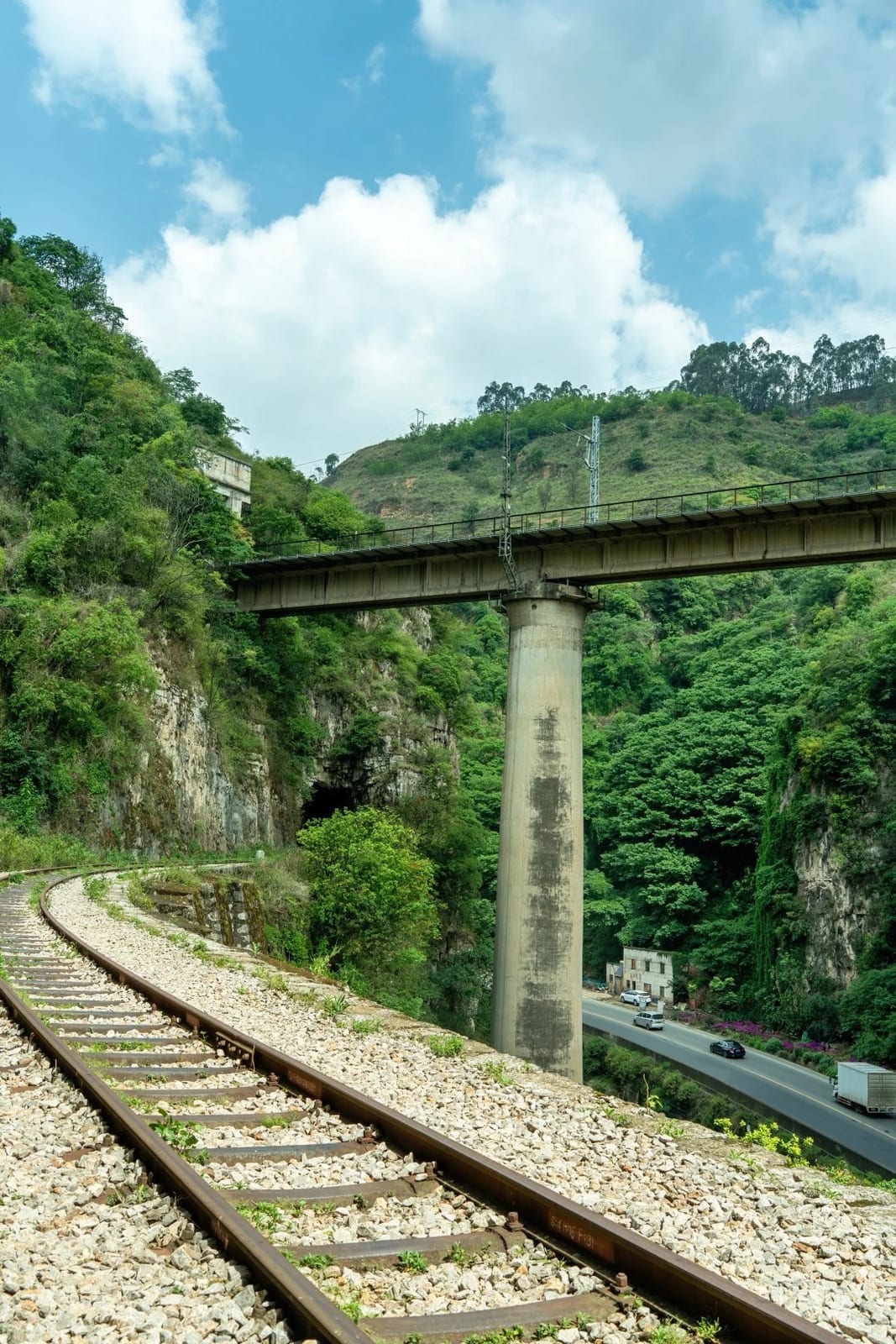 The Yunnan–Vietnam Railway curving beneath a tall concrete bridge, the valley road alongside, between Kebao and Yiliang