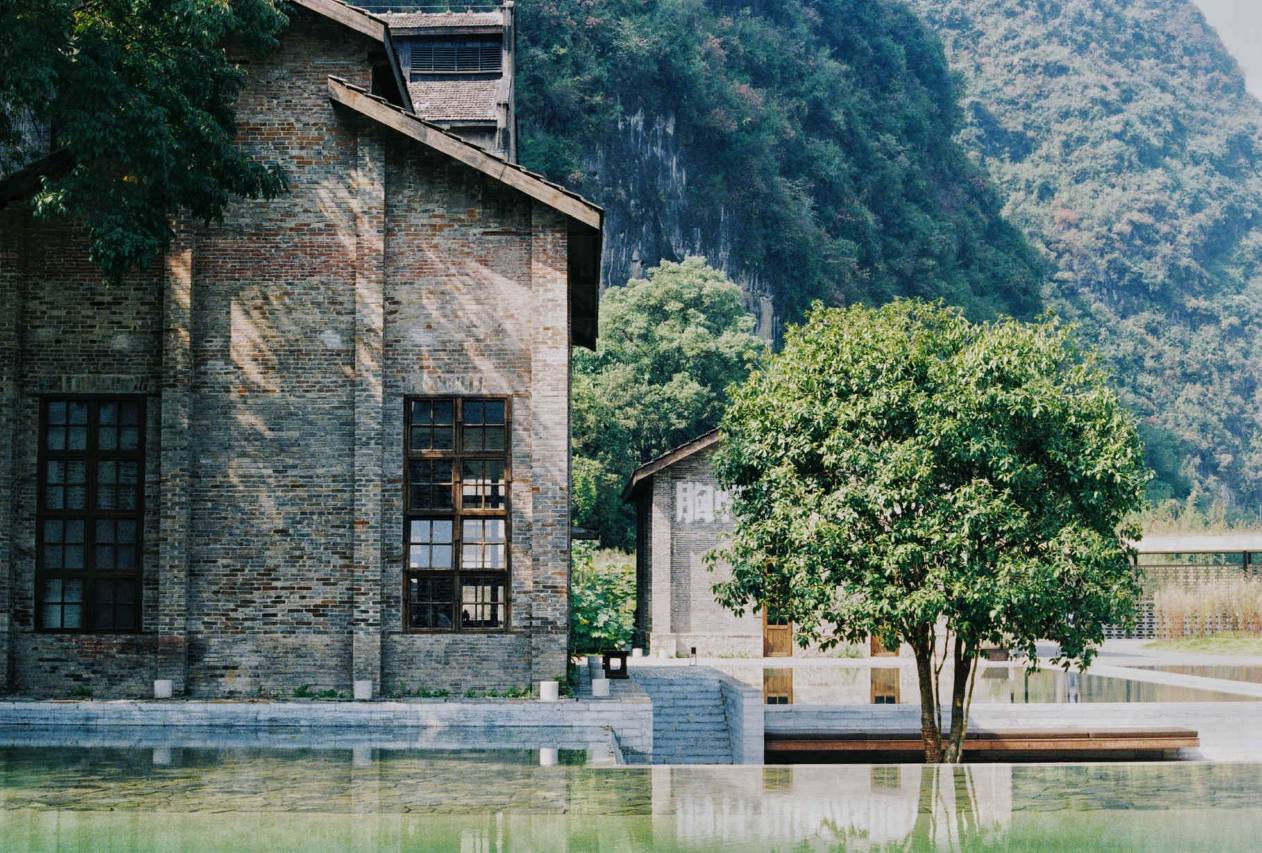 Alila Yangshuo — the preserved 1960s brick sugar-mill gable reflected in the water garden, karst backdrop, Yangshuo