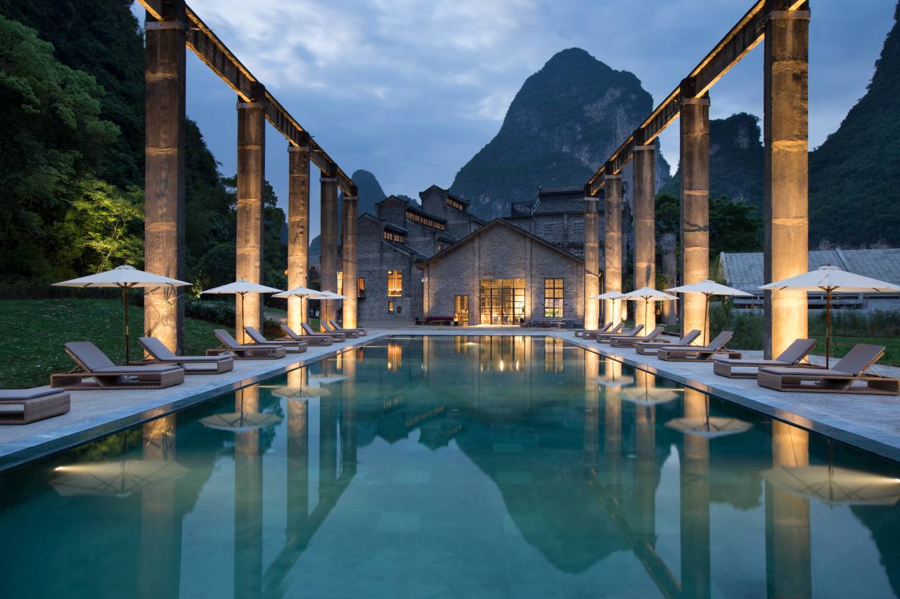 Alila Yangshuo — the cantilevered pool between the old sugar-mill's concrete columns at dusk, karst peaks behind, Li River