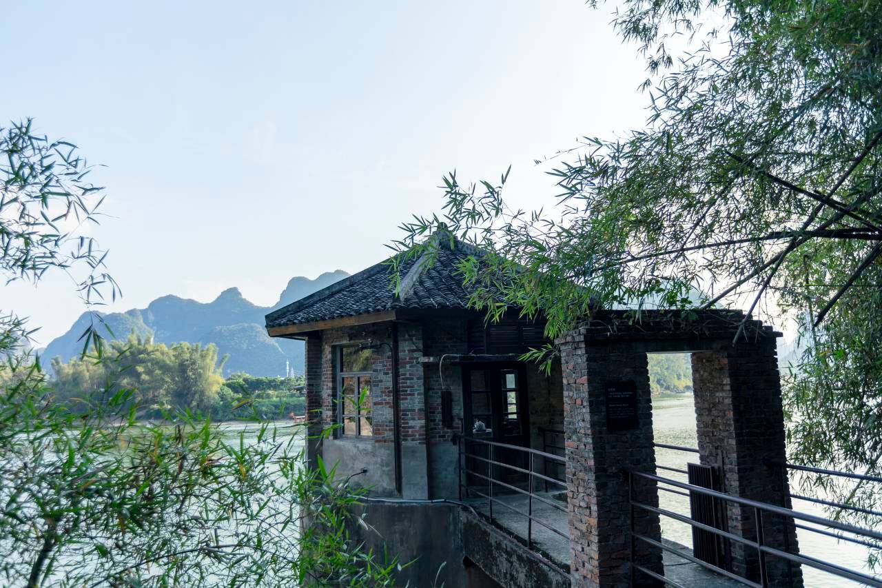 Alila Yangshuo — a brick riverside pavilion framed by bamboo above the Li River, karst peaks beyond