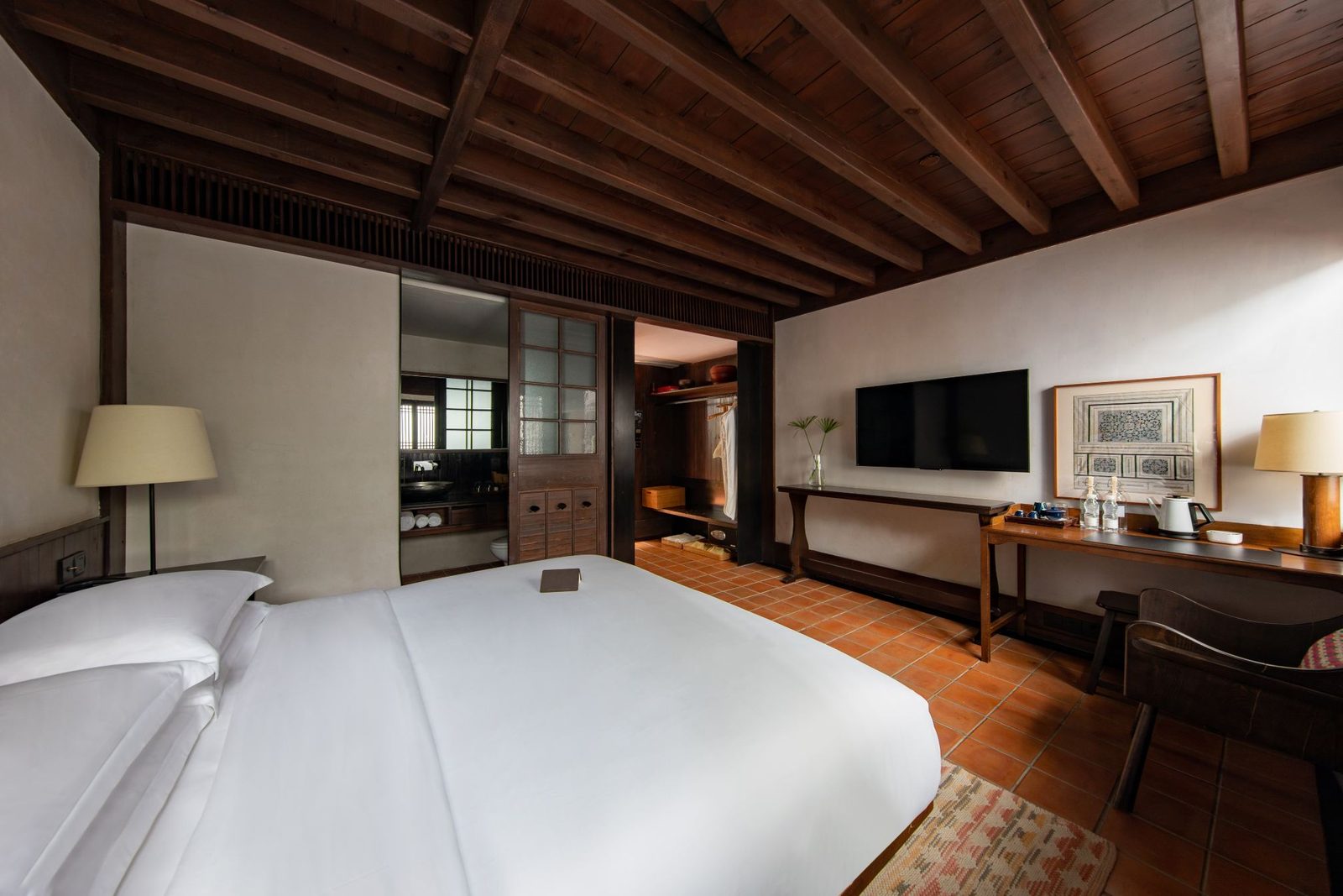 King room under a dark-beamed timber ceiling, white bedding, desk and a lattice window.