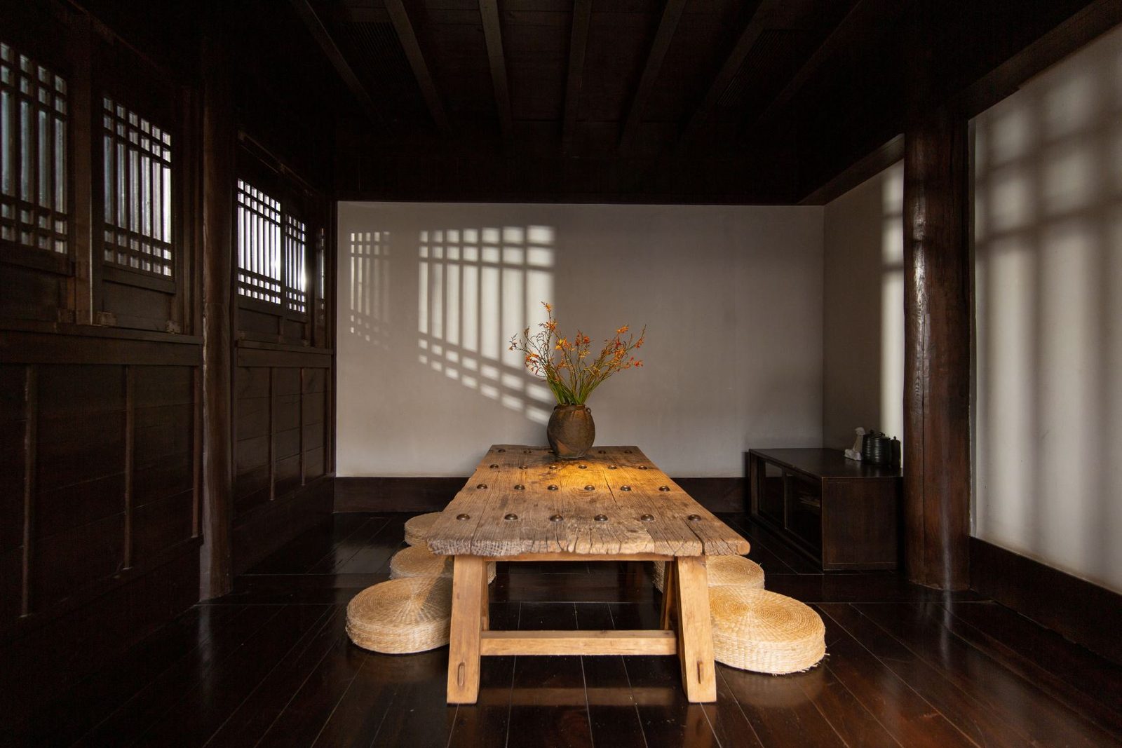 Tea room with a low old-timber table, straw floor cushions and lattice shadows on a white wall.
