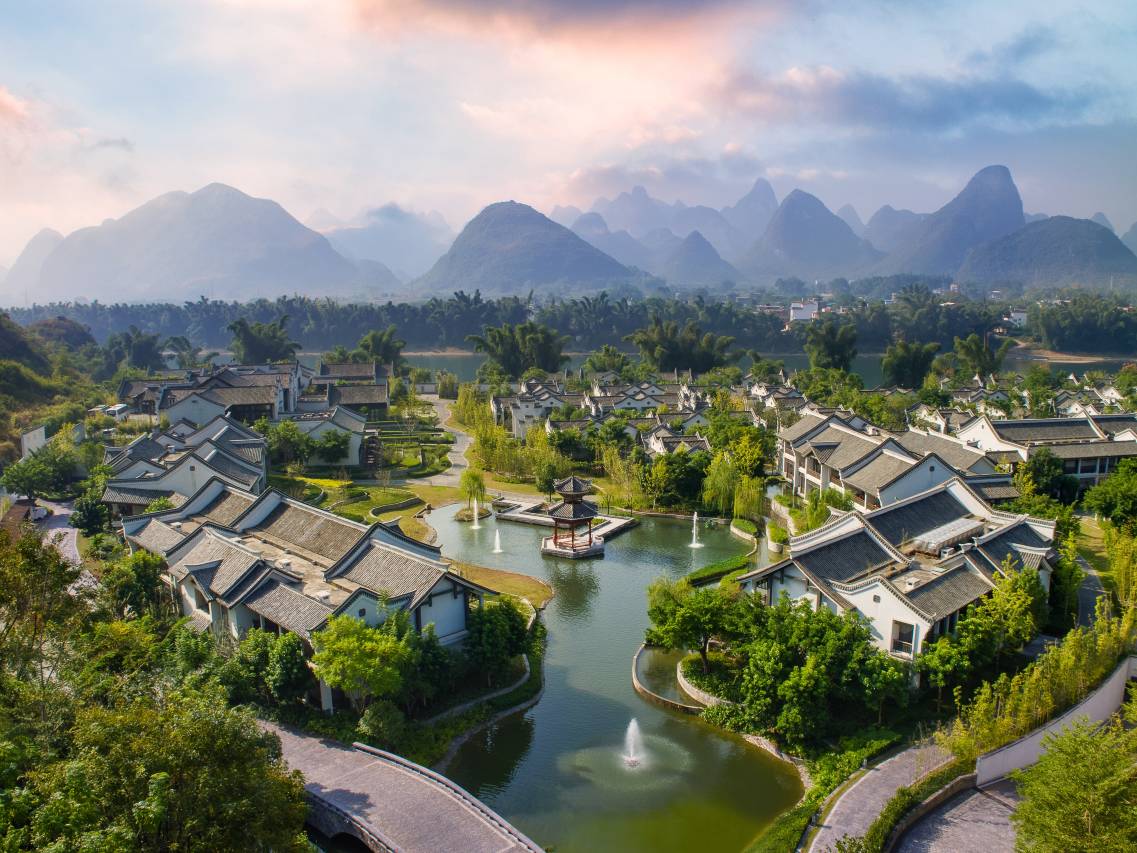 Banyan Tree Yangshuo — aerial over the lagoon, gardens and courtyard suites beneath the peaks