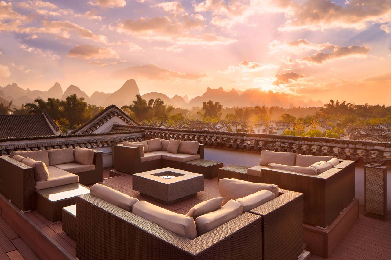 Banyan Tree Yangshuo — the rooftop sunset lounge above tiled gables, karst silhouettes at dusk