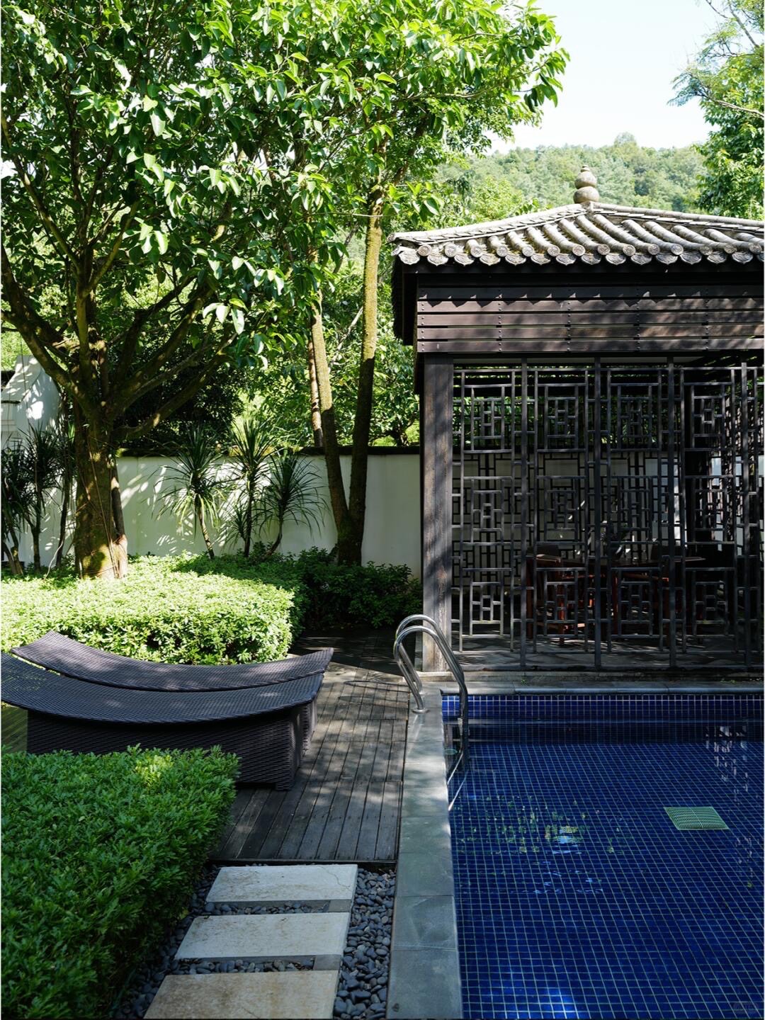 Blue-tiled private plunge pool with a curved lounger beside a lattice-screened garden pavilion and clipped hedges.