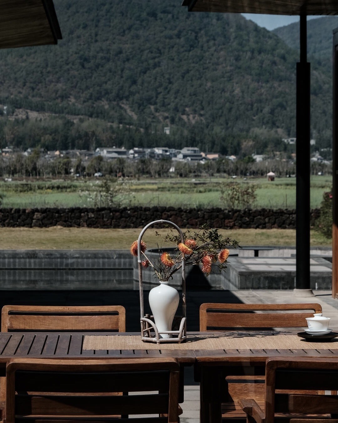 Terrace tea table with a white vase of orange blooms overlooking farmland and forested mountains.