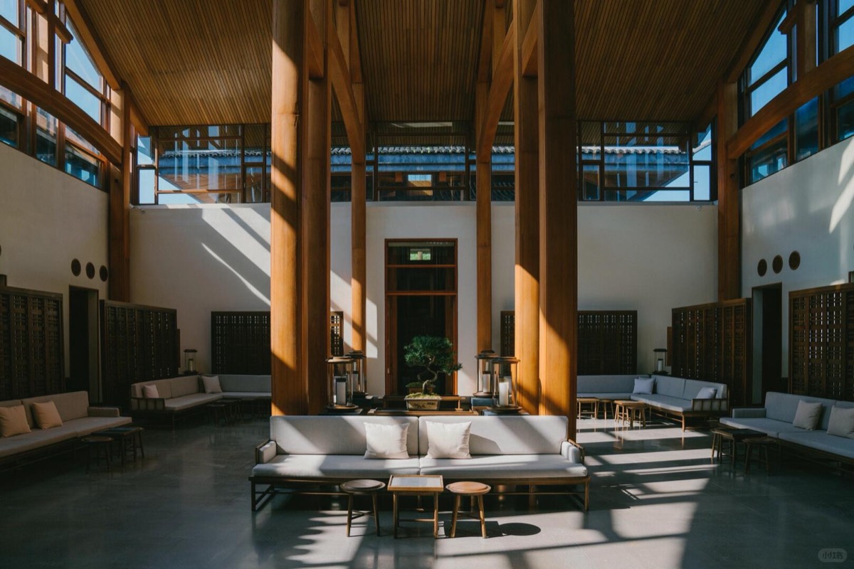 Sunlit timber-columned lobby atrium with white sofas arranged around a central bonsai display.