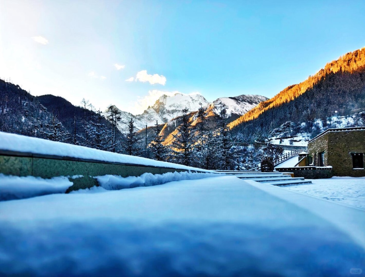 Fresh snow blanketing a terrace with sunlit forested mountains and a snow peak in the distance at Bore Yading.