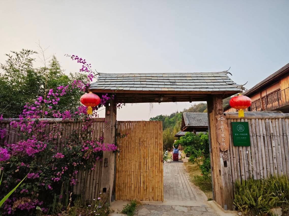 Bulang Yuni Inn — the timber entrance gate with red lanterns and bougainvillea, Wengwa hamlet, Mangjing