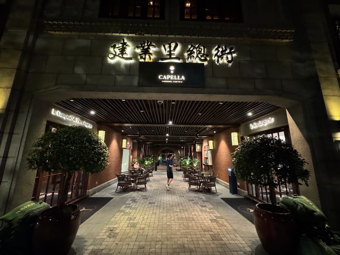 Capella Shanghai, Jian Ye Li — the stone gateway to Jian Ye Li lit at night, its name in Chinese characters above the Capella sign and a paved lane leading in past café tables