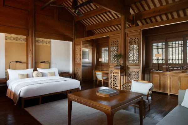 Spacious guestroom with dark timber beams, carved lattice screens and a white-linen bed at Dayanaman.