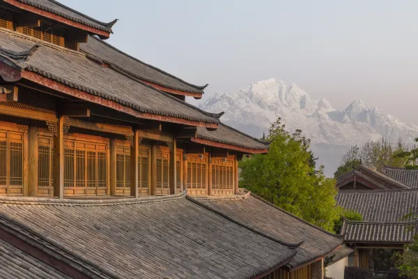 Golden-lit timber eaves and grey-tiled roofs with a distant snow peak at Dayanaman.