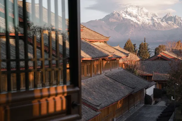 View from a timber window across warmly lit tiled rooftops to a snow-capped mountain at sunset at Dayanaman.