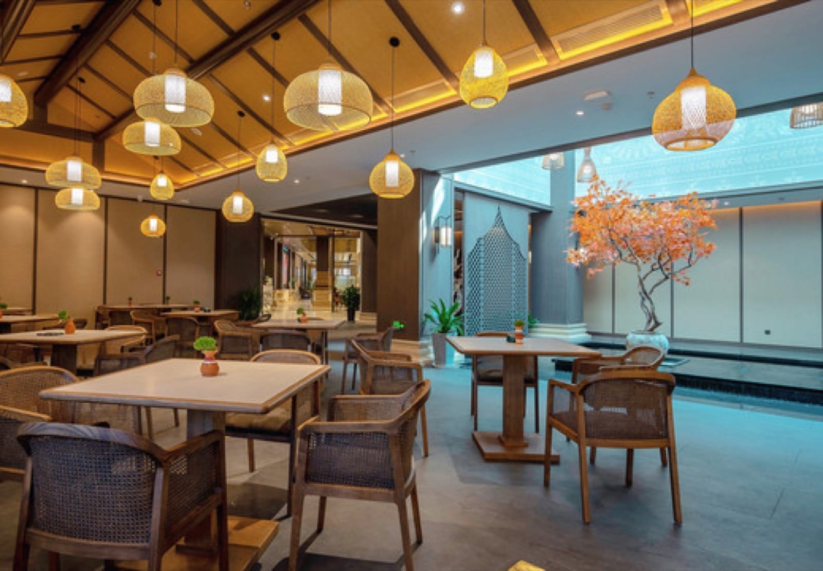 Fanshi Hotel — a light-filled restaurant under woven-bamboo pendant lanterns and a timber ceiling, rattan chairs and a blossom tree beside a reflecting pool