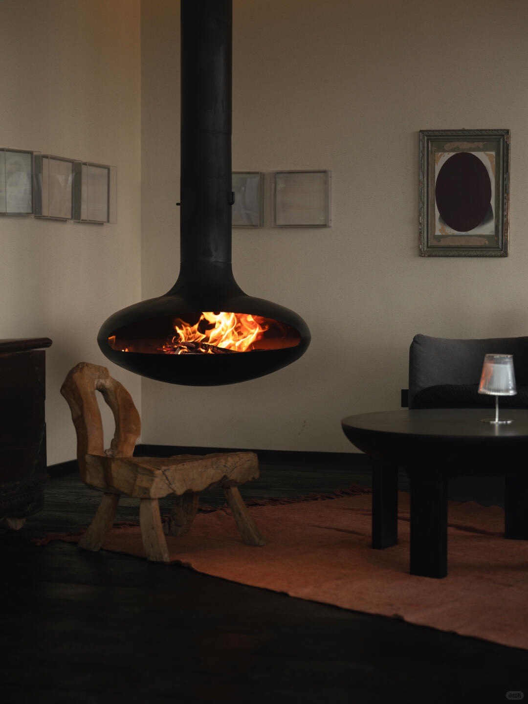Suspended black wood-burning fireplace beside a rustic carved timber chair on a rug in a warm lounge.
