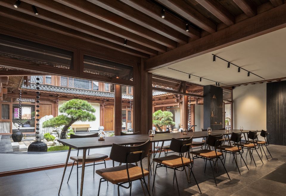 Kogongdi — glassed dining hall opening onto a planted courtyard with a single black-pine bonsai, Shaxi