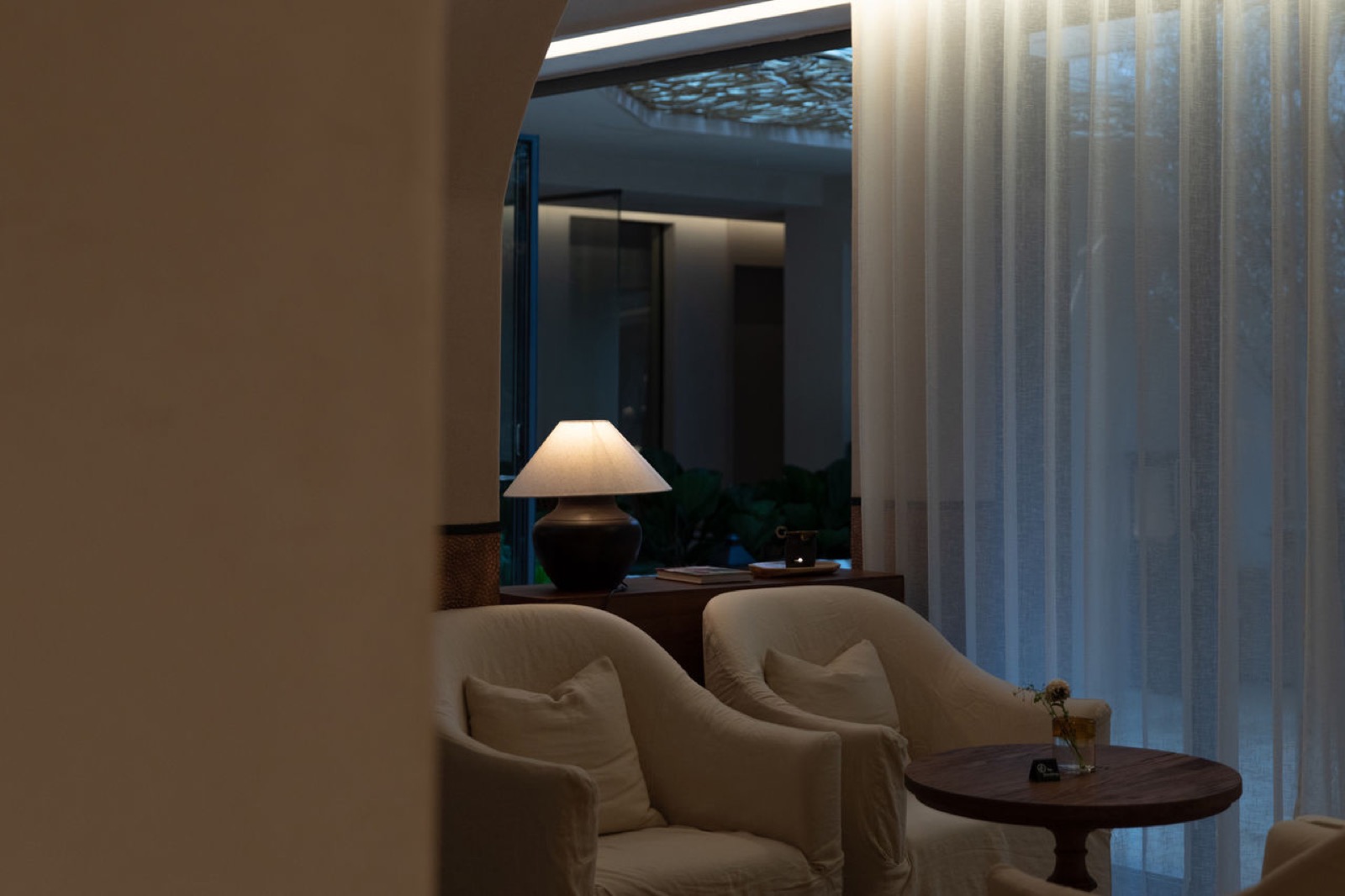 Luna Sea-View Inn — a quiet lounge corner at dusk with pale linen armchairs, a ceramic lamp and sheer curtains