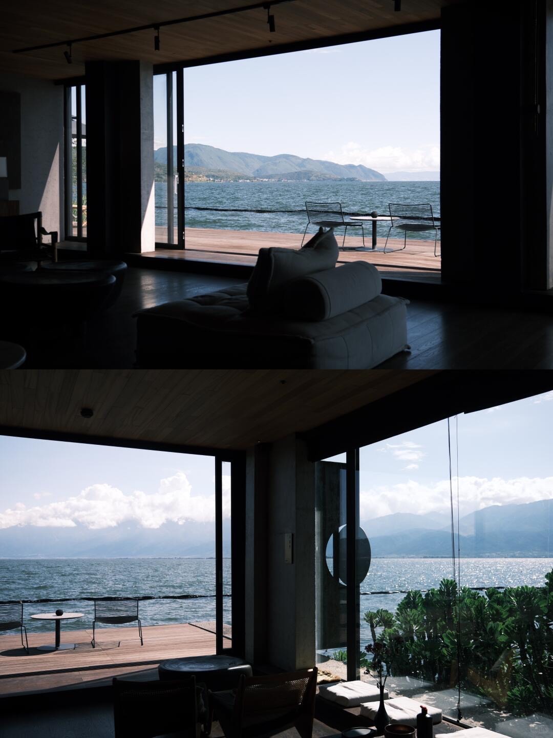 Dim lakefront living room looking out through wide glass doors to a wooden deck with chairs beside the water.
