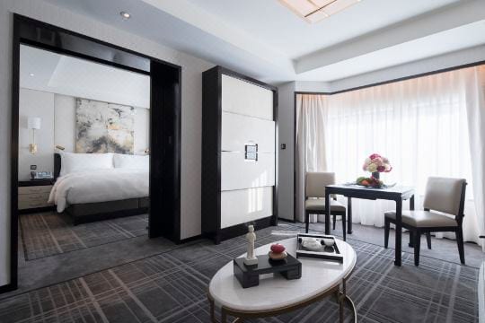The Peninsula Beijing — a Superior Suite's sitting room, a writing table by sheer-curtained windows and the bedroom through a dark-framed doorway