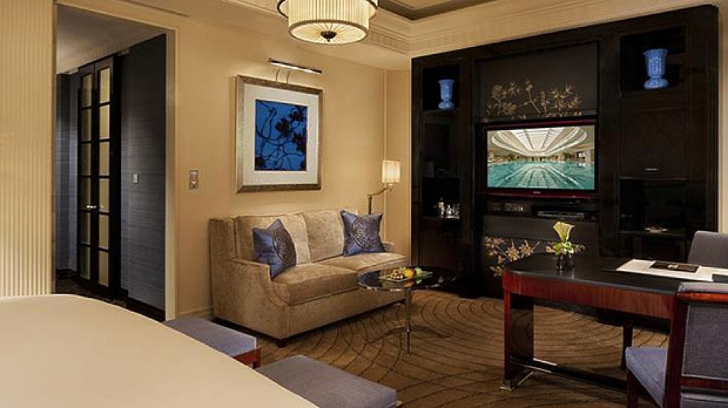 The Peninsula Shanghai — the sitting area of a Deluxe Room, a sofa beneath framed art and a black lacquer cabinet painted with gold blossom