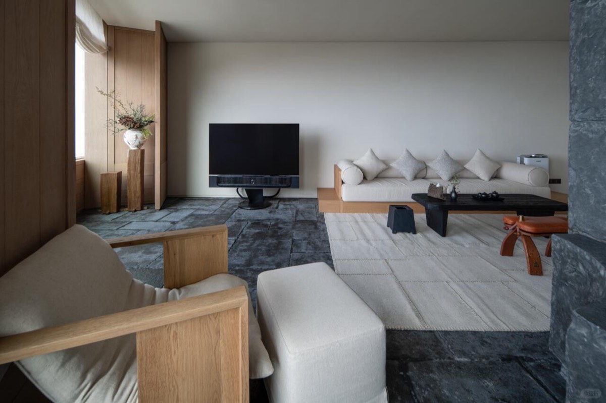 Minimalist suite living room with pale sofa, low black table and stone-slab flooring beside a wood-panelled wall.