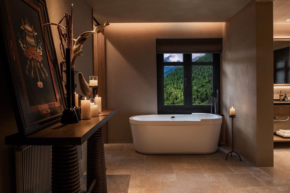 Candlelit bathroom with a freestanding tub framed by a window overlooking a forested mountain slope.