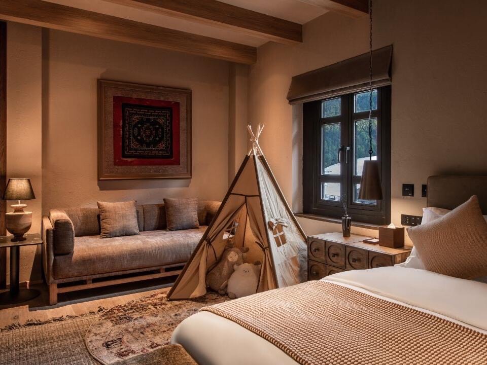 Cosy bedroom with a canvas play teepee, soft sofa, framed textile and window onto forested hills.