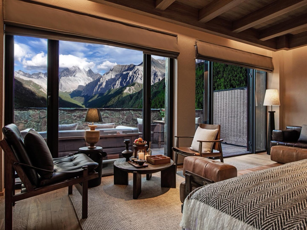 Suite lounge with leather chairs facing floor-to-ceiling windows over a snow-capped mountain valley.