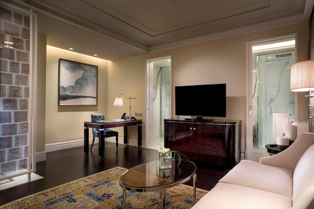 Sofitel Legend People's Grand Xi'an — a sitting area with a lacquered desk beneath an ink-wash painting, a glass screen printed with carved-brick motifs and a marble bathroom through the sliding door