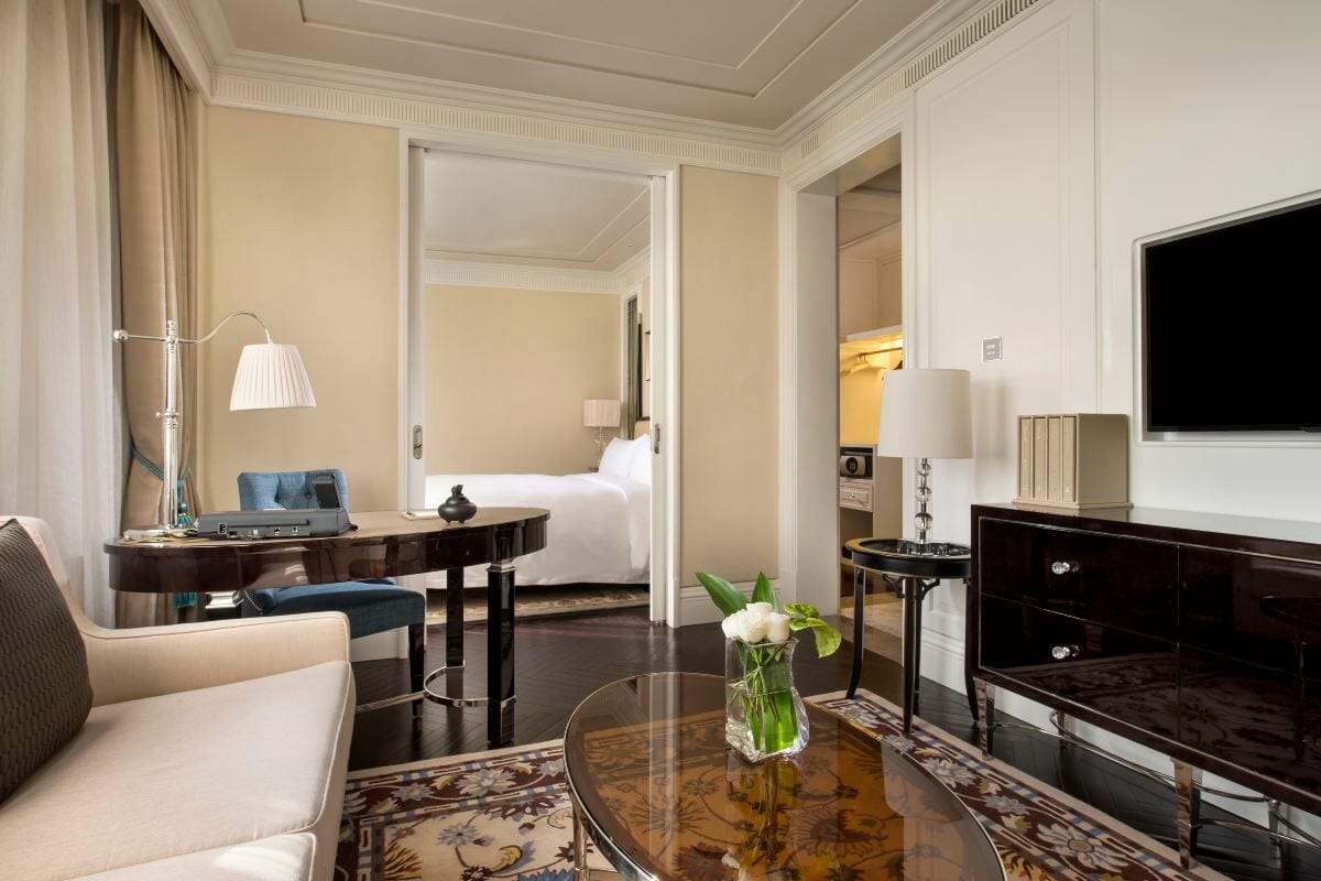 Sofitel Legend People's Grand Xi'an — a suite sitting room, a writing desk and blue chair by the window, white roses on a glass table and sliding doors open to the bedroom