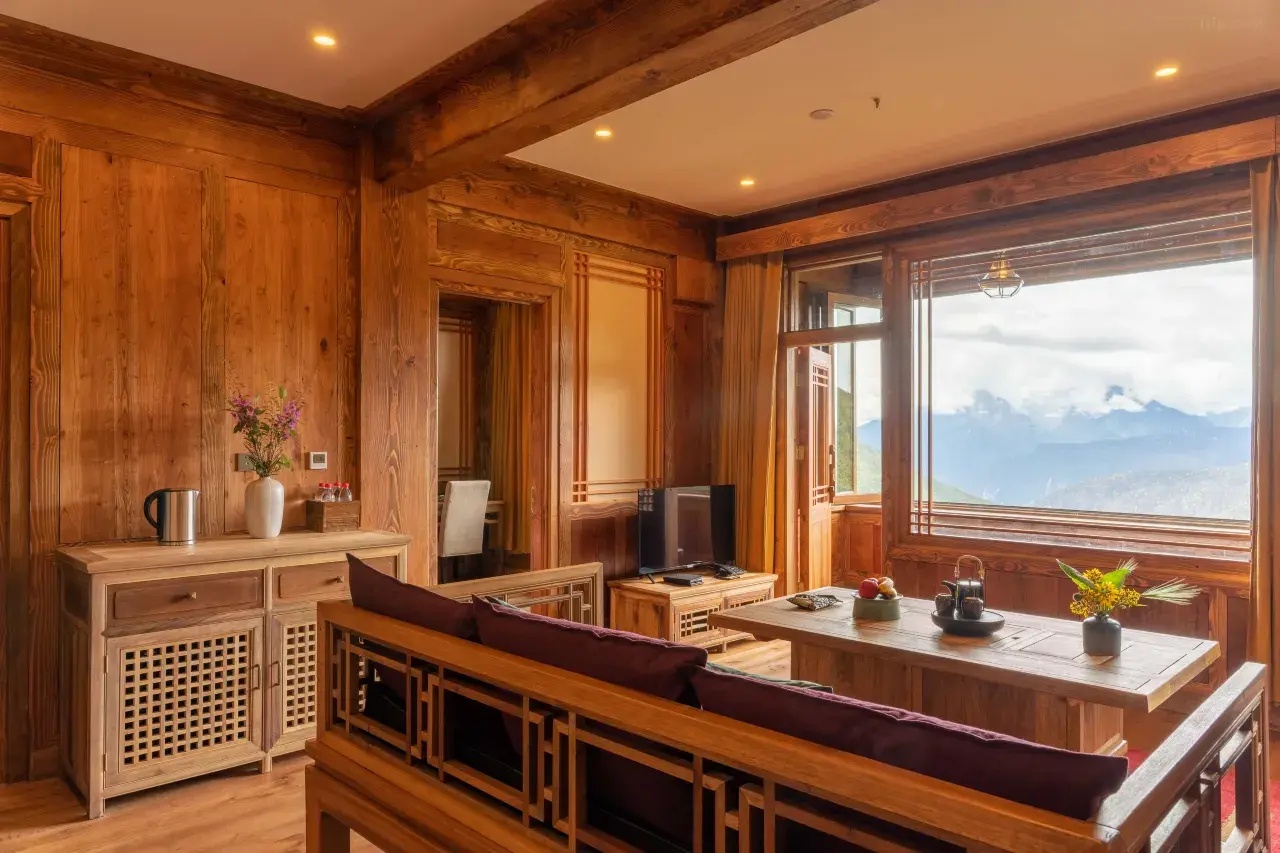 Timber-panelled Tibetan-style suite with a bench seat and a picture window framing distant cloud-wrapped mountains.