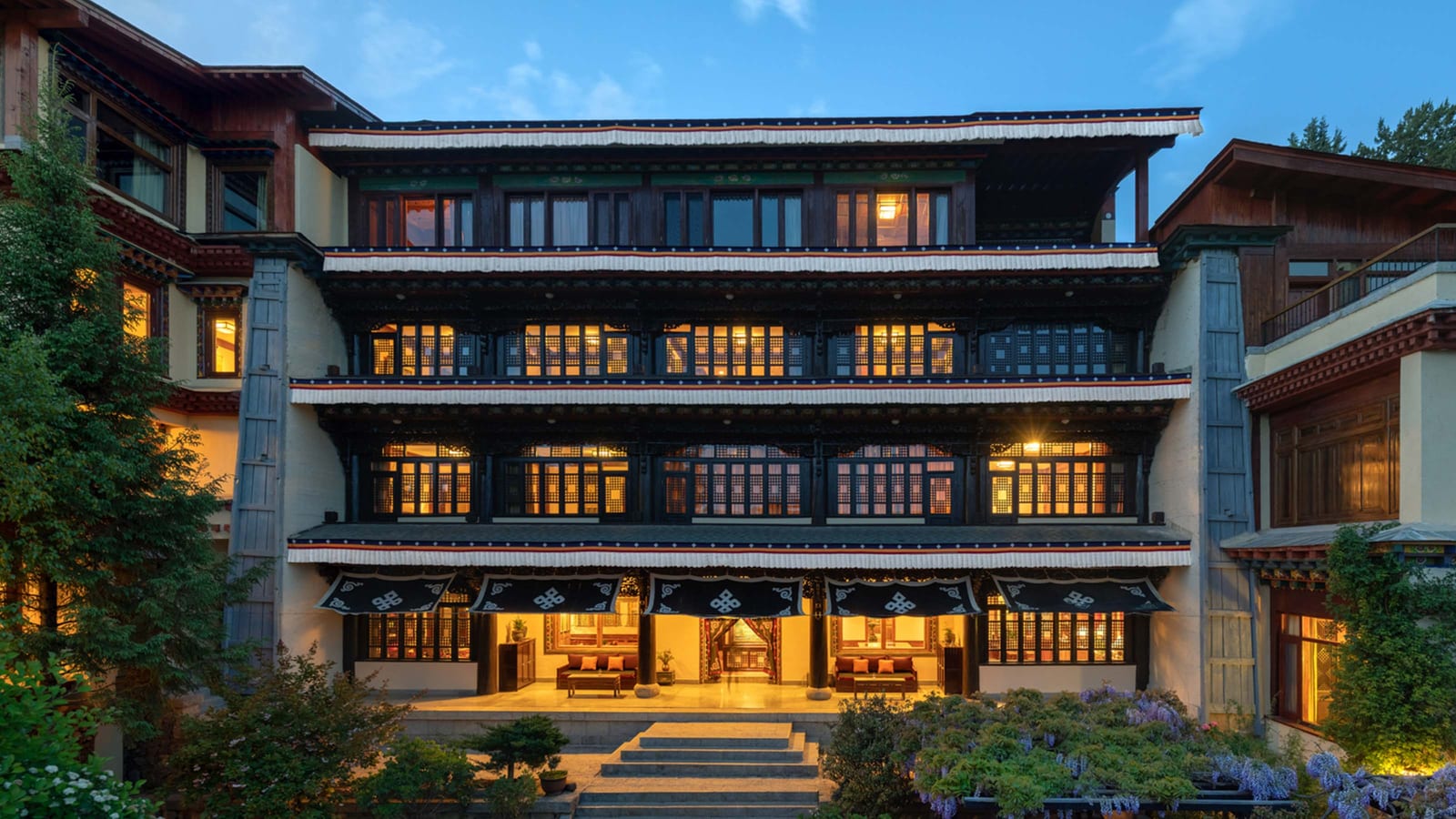 Songtsam Lodge Shangri-La (松赞绿谷山居) — the four-storey Tibetan lodge at dusk, lattice windows lit beneath white-fringed eaves