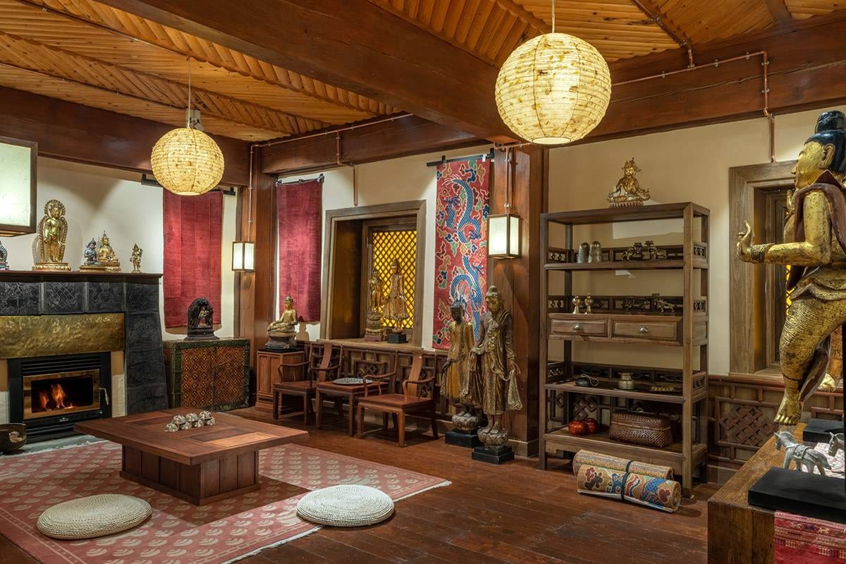 Songtsam Lodge Shangri-La — a lounge of gilded Buddhist figures and red woven hangings, a fire lit in the stone hearth