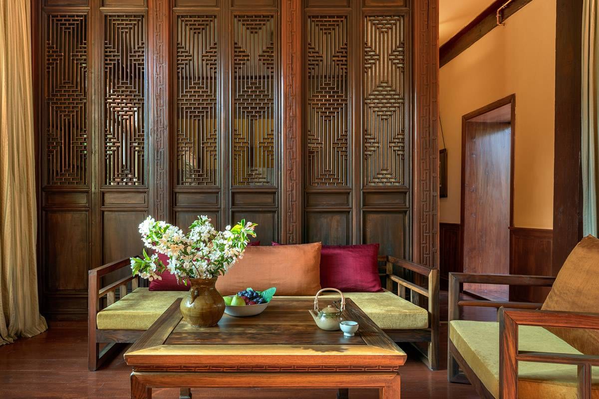 Songtsam Lodge Shangri-La — a timber daybed with ochre and crimson cushions before tall carved lattice screens, white blossom, fruit and a teapot on the low table